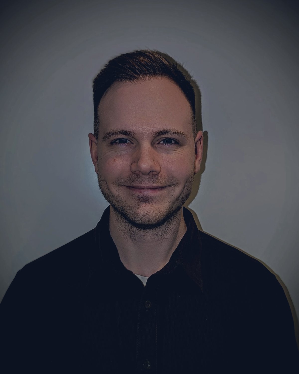 Portrett av Marcus Larsen som smiler, i mørk skjorte mot en grå vegg.